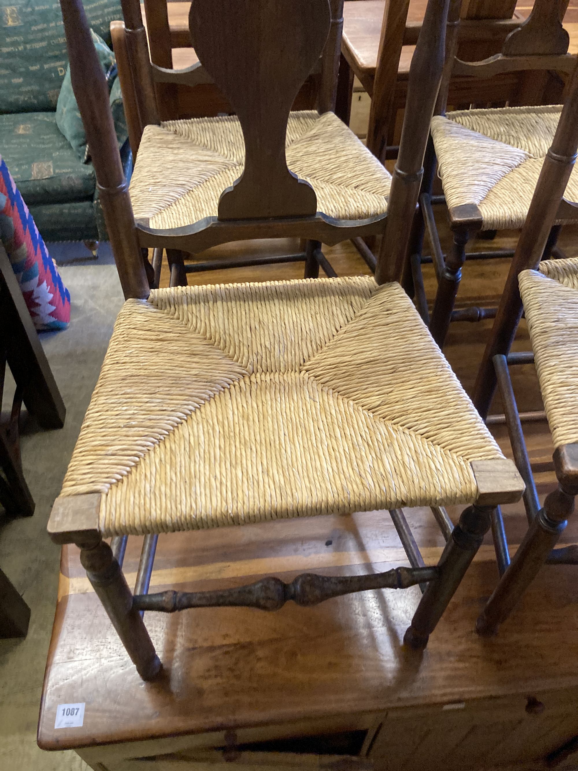 A set of four George III country oak rush seated chairs, with shaped back splat, turned supports and stretchers